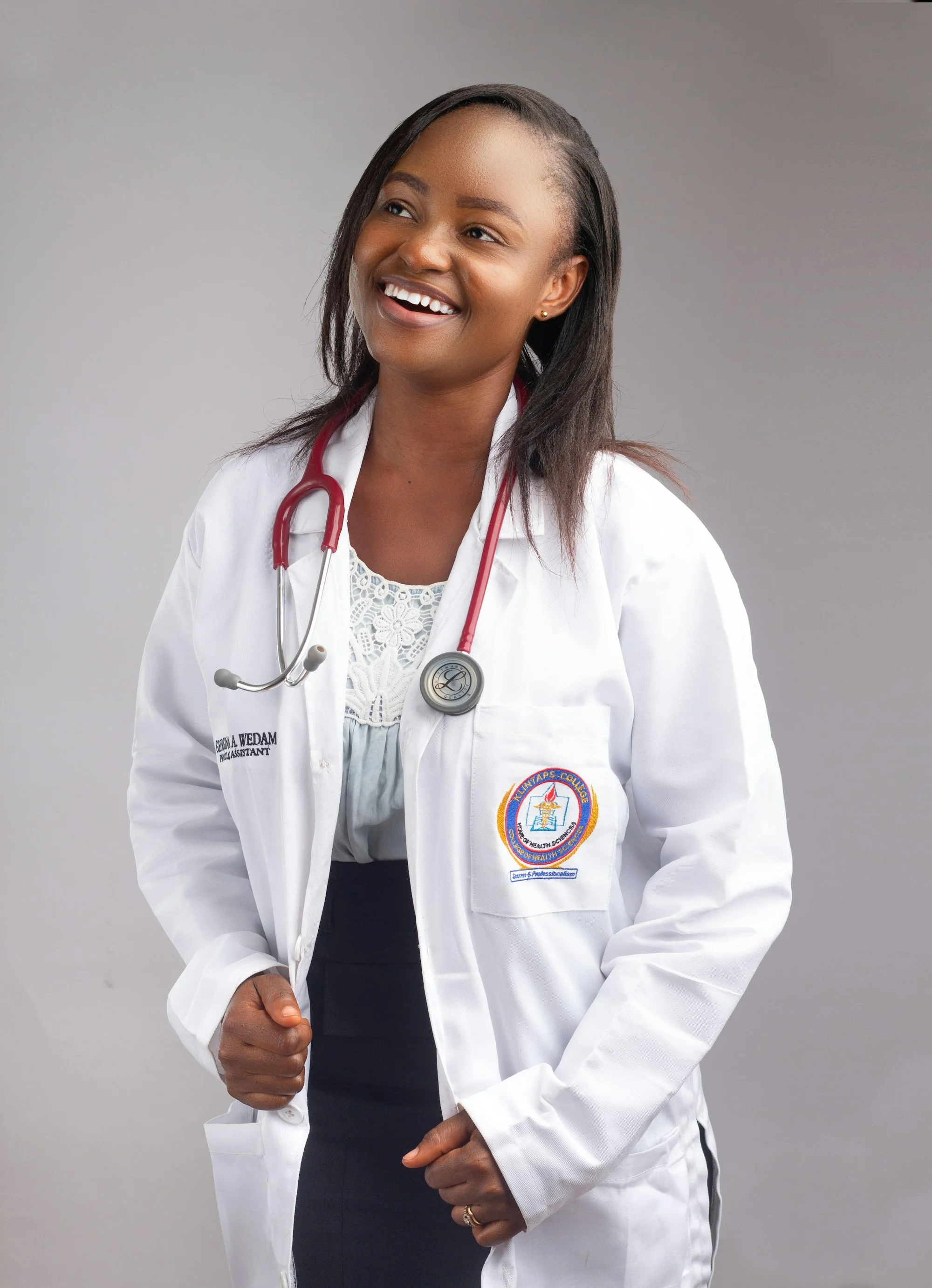 A clinician in a white coat with a stethoscope, smiling warmly in a studio portrait.
