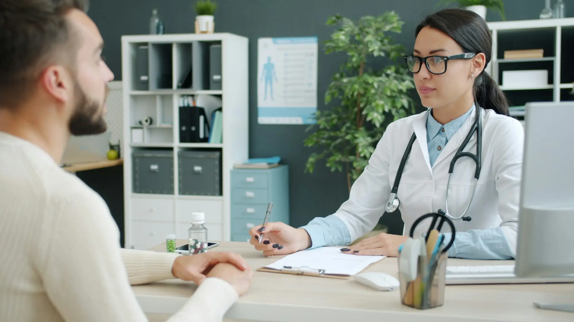 A doctor in a modern clinic consulting with a male patient across a desk.