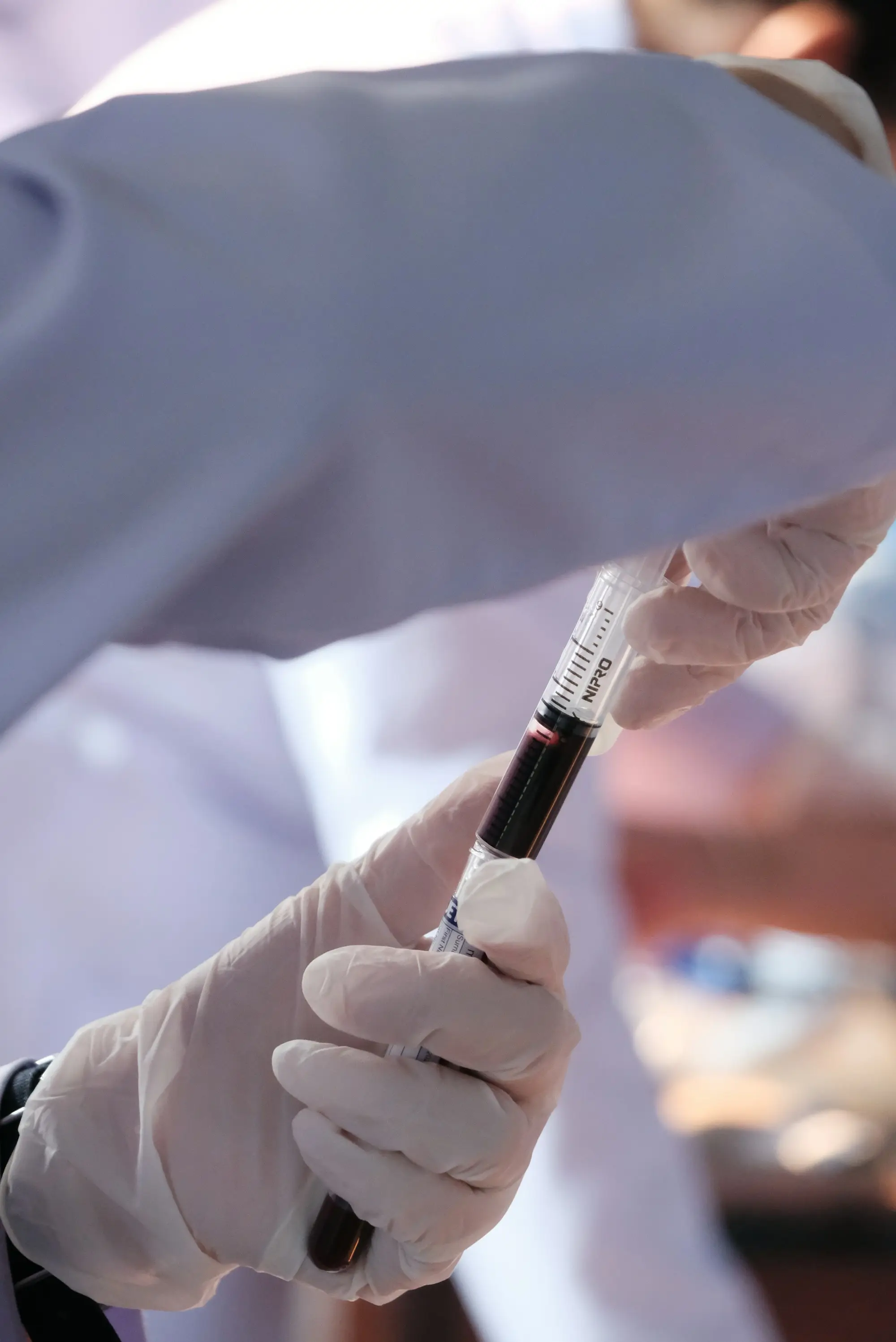 A gloved hand inserts a sample tube of blood into a labelled holder in a modern clinical lab.