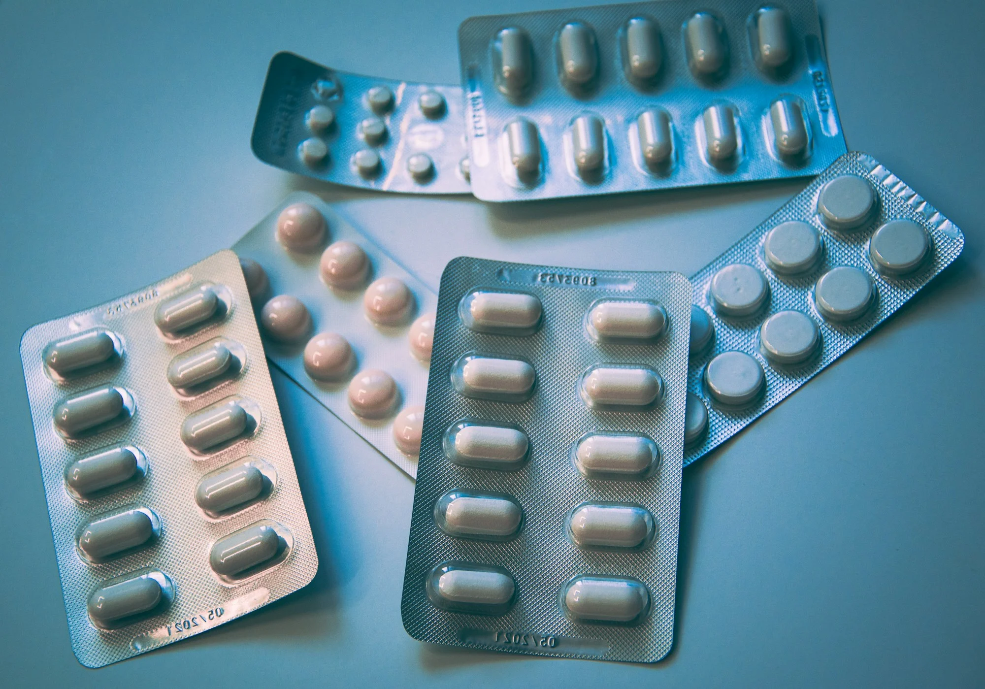 Several blister packs of pills and capsules arranged on a soft blue background.