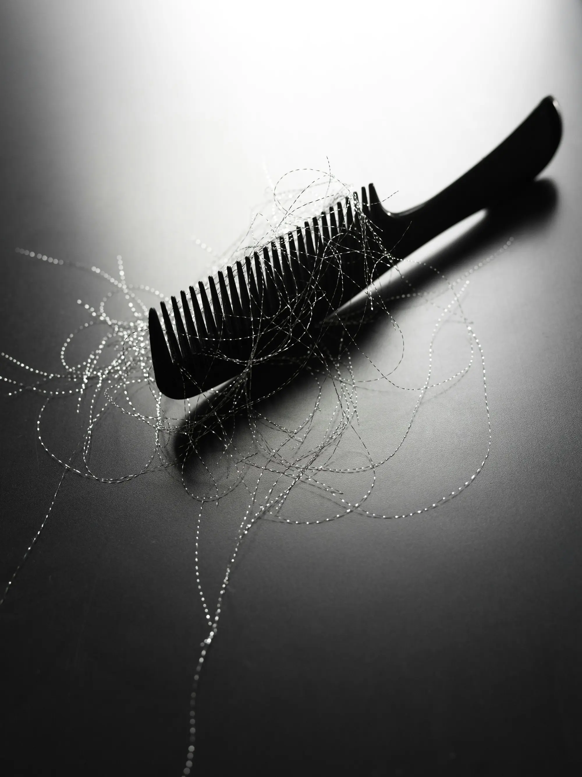 A black comb with shed hair strands tangled in its teeth, on a dark backdrop.